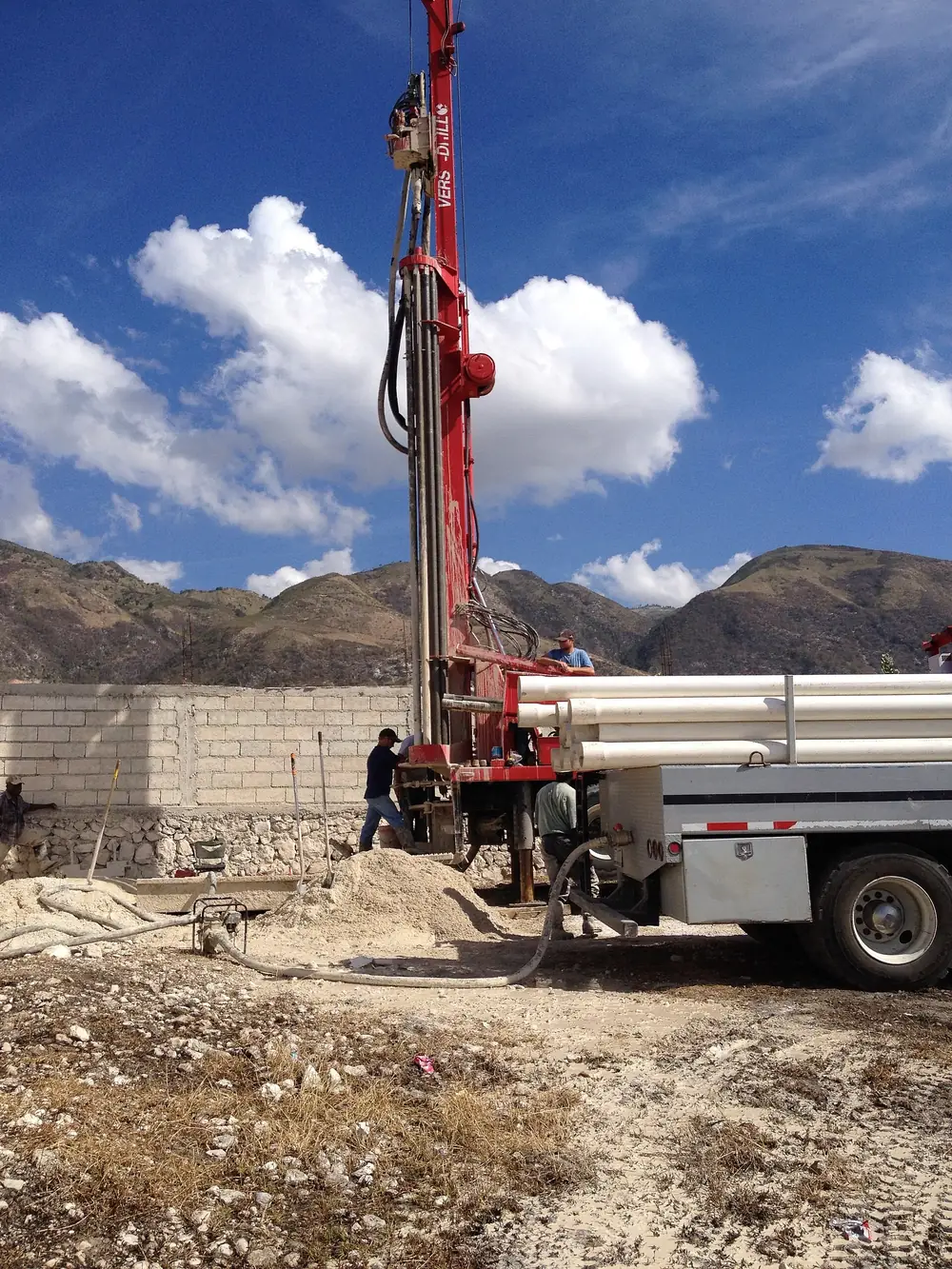 A borehole drilling rig at work on dry ground under a blue sky